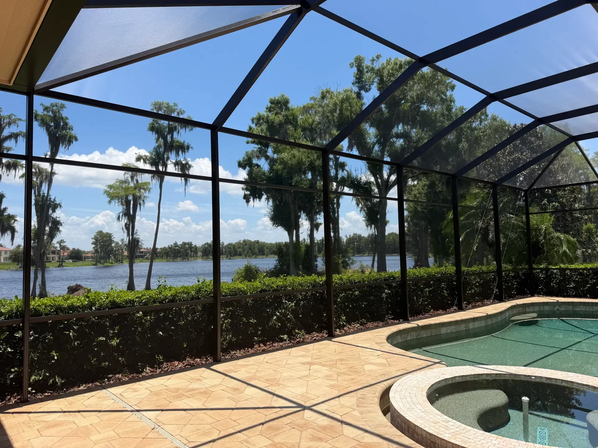 Large luxury black-frame pool enclosure with taut new screening overlooking a lake
